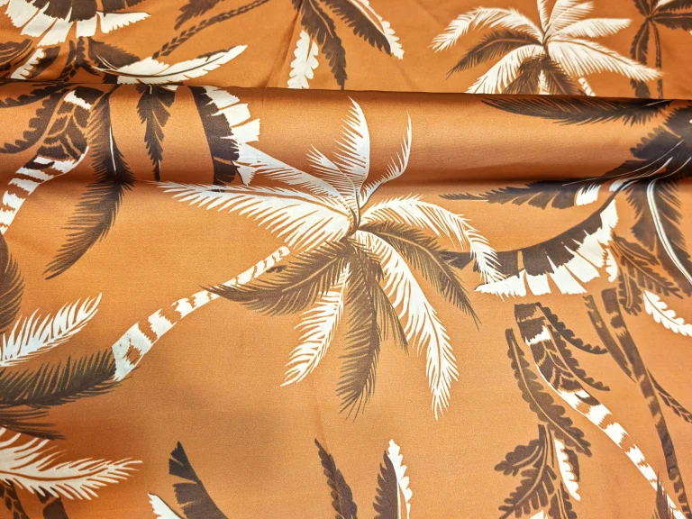 Țesătură tip saten pe fond muștar cu palmieri ivoire și model multicolor, material din poliester 100% pentru rochii, bluze și fuste, lățime 140 cm, import Italia