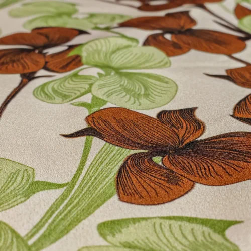 Detaliu de țesătură din mătase naturală Crepe de Chine, cu model repetitiv de orhidee în nuanțe de verde și maro, textură ușor ondulată și cădere fluidă