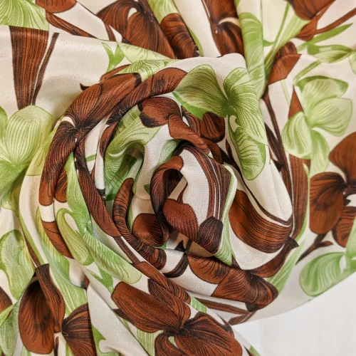 Țesătură din mătase naturală 100% Crepe de Chine, cu model repetitiv orientat pe lungimea materialului, imprimeu floral cu orhidee verzi și maro pe fond alb, ideală pentru rochii și salopete