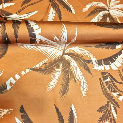 Țesătură tip saten pe fond muștar cu palmieri ivoire și model multicolor, material din poliester 100% pentru rochii, bluze și fuste, lățime 140 cm, import Italia